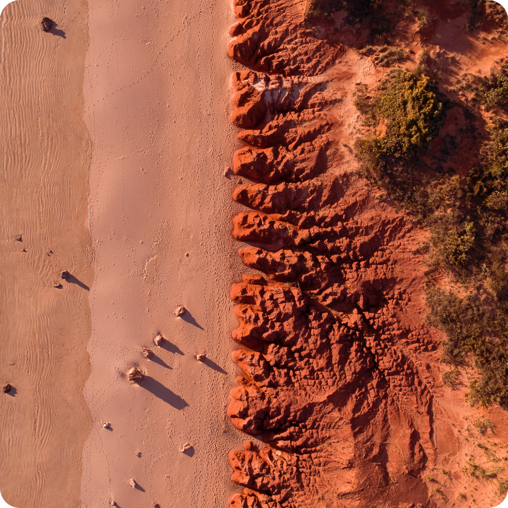 Aerial view of a red sandy beach with rugged, eroded cliffs.